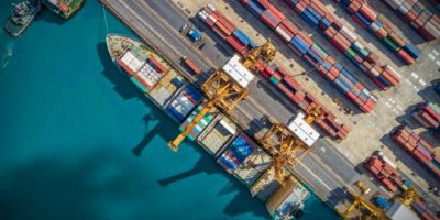LkSG: Bunte Containerschiffe im Hafen bei Sonnenschein