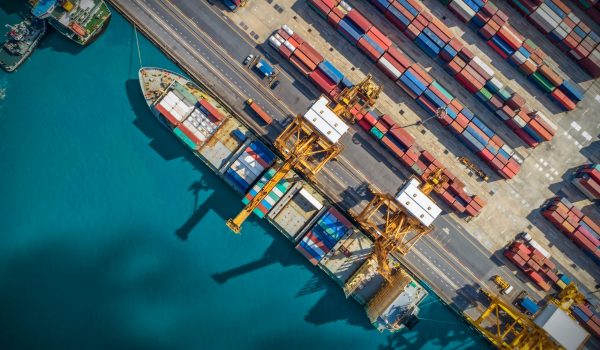 LkSG: Bunte Containerschiffe im Hafen bei Sonnenschein
